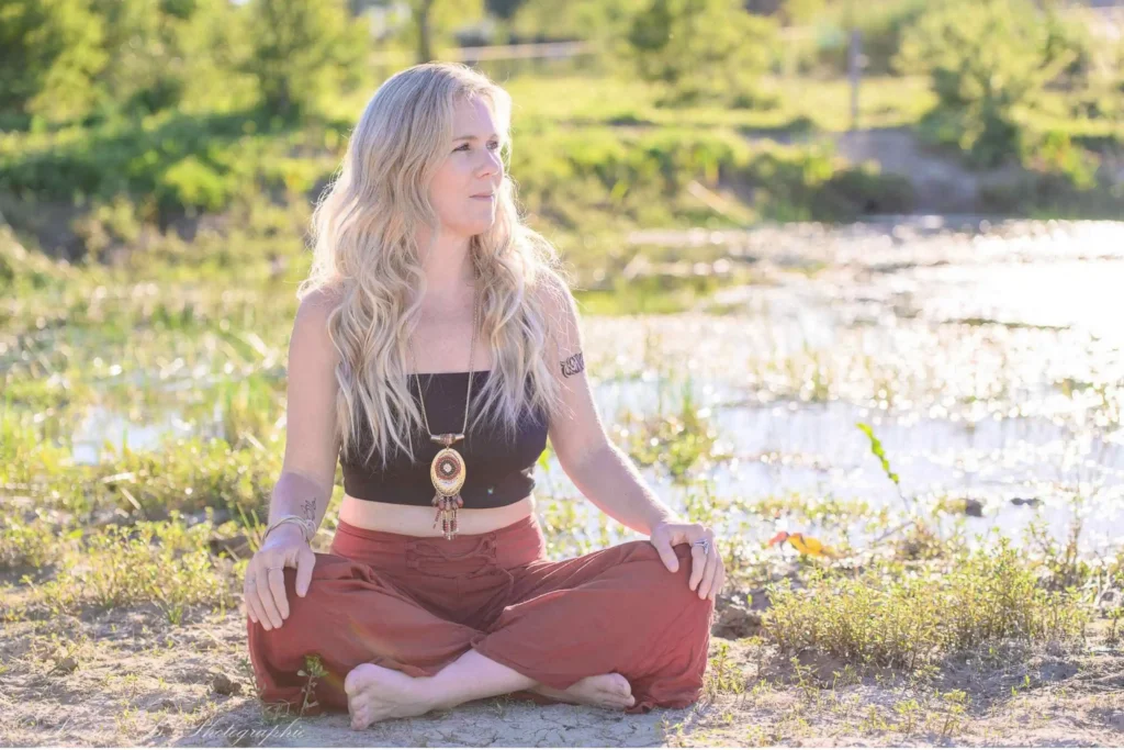Cypriane Guyot assise en tailleur près d'un étang les mains posées sur ces genoux contemplant l'horizon